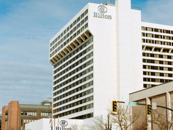 White Hilton hotel building with logo on the corner, urban street in foreground and blue sky above