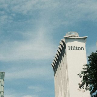 White Hilton hotel tower with rounded top and vertical fins against a blue sky.