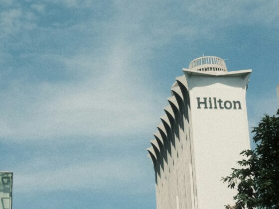 White Hilton hotel tower with rounded top and vertical fins against a blue sky.