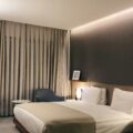 Hotel bedroom with a large white bed, beige throw, and wooden platform under warm ambient lighting.