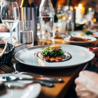 Plate with greens and sauce beside a bread basket at a candlelit restaurant table, ready to be served.