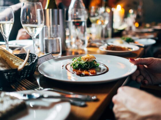 Plate with greens and sauce beside a bread basket at a candlelit restaurant table, ready to be served.