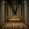 Long, dim hotel hallway with doors on both sides and warm overhead lights, extending toward a distant exit sign.