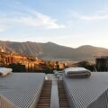 Poolside lounge chairs with striped cushions facing a mountain range under a clear blue sky at sunset.