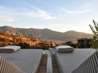 Row of striped lounge chairs with folded towels at a desert resort, mountains in the background.
