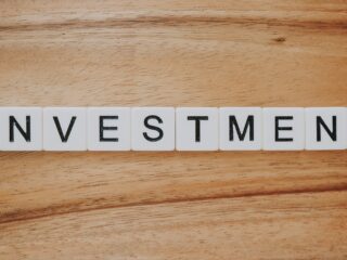 Tiles spell out the word INVESTMENT on a wooden surface