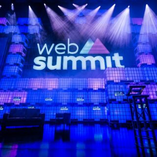Stage at Web Summit with large logo and blue lighting, stacked cube structures on either side of the screen.