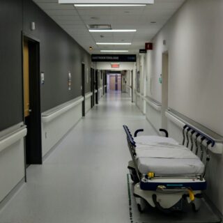 Empty hospital hallway with a wheeled patient stretcher in the foreground and overhead signs guiding to Urology and other departments