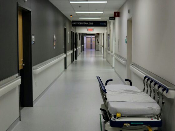 Empty hospital hallway with a wheeled patient stretcher in the foreground and overhead signs guiding to Urology and other departments