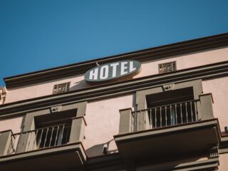 Pink hotel exterior with a white oval 'HOTEL' sign on a peach wall beneath a clear blue sky.
