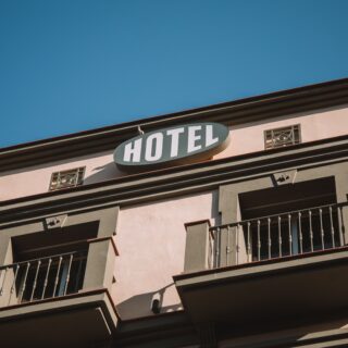 Pink hotel exterior with a white oval 'HOTEL' sign on a peach wall beneath a clear blue sky.