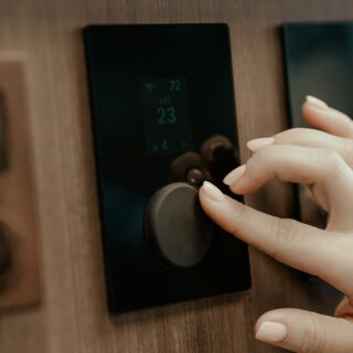 Close-up of a hand pressing a code on a touchscreen door lock mounted on a wooden door surface.