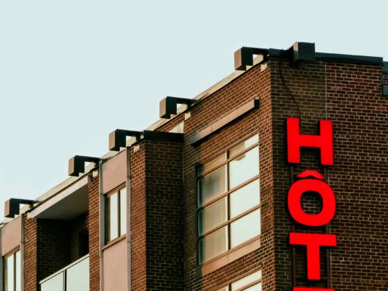 Brick building with large red vertical letters spelling HOTEL on its facade, against a pale blue sky.