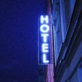 Vertical blue neon hotel sign mounted to a building at night, partially visible letters forming 'HOTEL'.