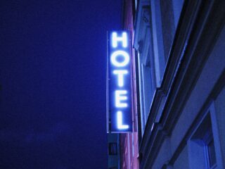 Vertical blue neon hotel sign mounted to a building at night, partially visible letters forming 'HOTEL'.
