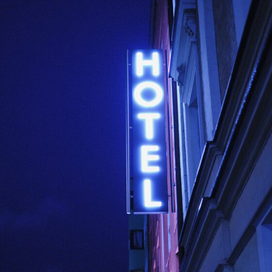Vertical blue neon hotel sign mounted to a building at night, partially visible letters forming 'HOTEL'.