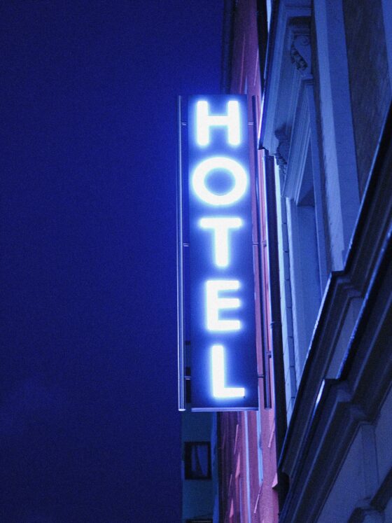 Vertical blue neon hotel sign mounted to a building at night, partially visible letters forming 'HOTEL'.