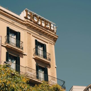 Beige European-style apartment building with black wrought-iron balconies and decorative stonework, clear blue sky above.