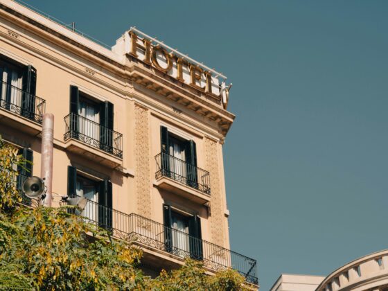 Beige European-style apartment building with black wrought-iron balconies and decorative stonework, clear blue sky above.