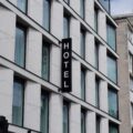 Modern glass-fronted hotel building with white paneling and a tall vertical black sign reading HOTEL.