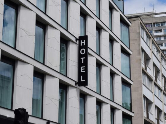 Modern glass-fronted hotel building with white paneling and a tall vertical black sign reading HOTEL.
