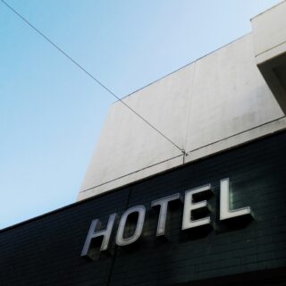 Close-up of a pale building facade with a partial 'HOTEL' sign on a dark green storefront against a clear blue sky.
