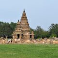 Stone tiered temple tower with a pointed top, set in a grassy area with visitors nearby.