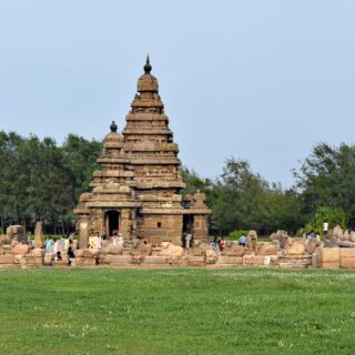 Stone tiered temple tower with a pointed top, set in a grassy area with visitors nearby.