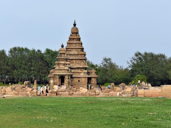 Stone tiered temple tower with a pointed top, set in a grassy area with visitors nearby.