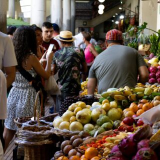 Indoor market scene with fruit stalls and shoppers; baskets of mangoes, dragon fruit, and oranges in the foreground.