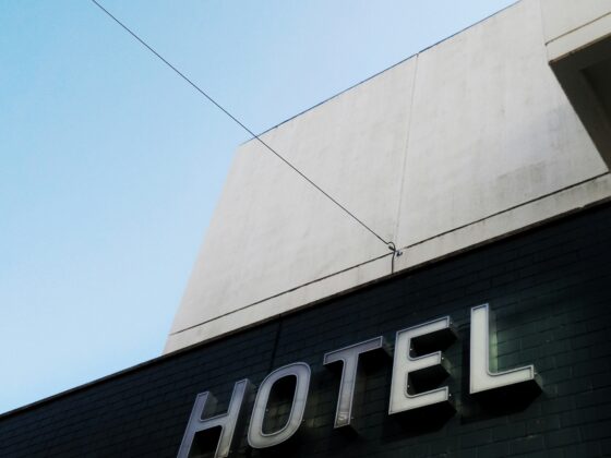 Partial view of a hotel sign on a dark green storefront under a pale blue sky; a power line crosses the frame.