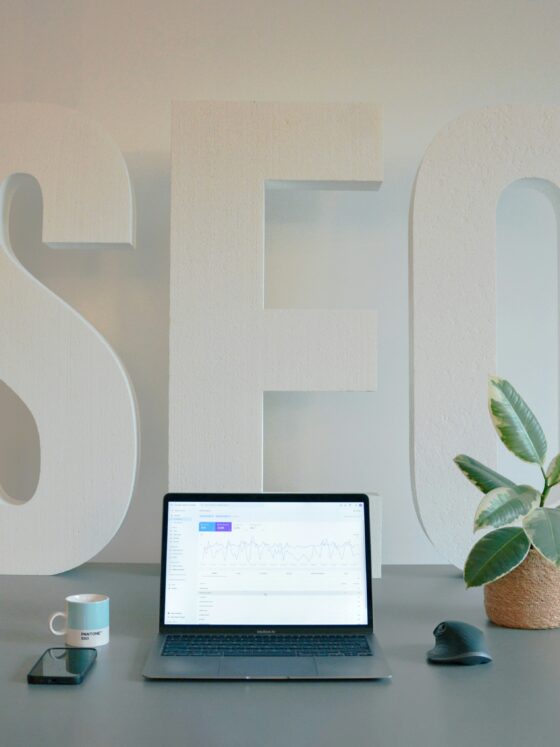 Large white 3D letters spell 'SELF' on a desk with a laptop, mug, phone, and plant nearby.