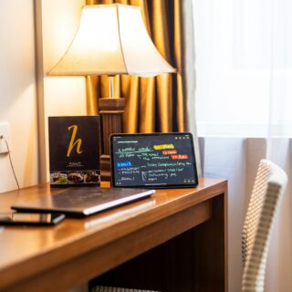 Desk corner with a tablet showing colorful chalkboard notes, a warm lamp, and gold curtains in the background, plus a woven chair nearby