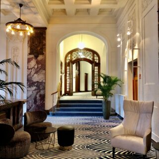 Luxurious hotel lobby with ornate coffered ceiling, arched wood doors, cozy seating, and a bold black-and-white wave carpet.
