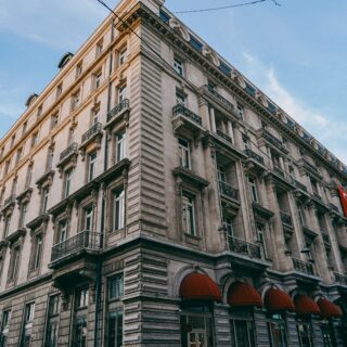Historic corner building with ornate balconies and red awnings along a city street under a clear blue sky; Turkish banners hang outside.