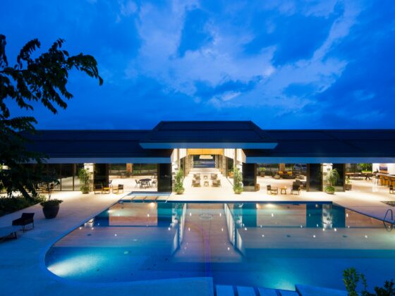 Hotel pool terrace at night with glass-walled lobby and warm seating illuminated along the pool edge