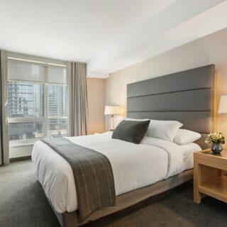 Hotel room with a large upholstered headboard, bed, two nightstands with lamps, and a city view through the window.