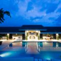 Hotel pool area at night with illuminated pool and open-air lounge spaces inside a glass-walled building under a blue sky