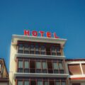 Low-angle view of a beige hotel building with a bright red 'HOTEL' sign on the roof against a clear blue sky.