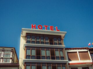 Low-angle view of a beige hotel building with a bright red 'HOTEL' sign on the roof against a clear blue sky.