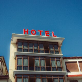 Low-angle view of a beige hotel building with a bright red 'HOTEL' sign on the roof against a clear blue sky.