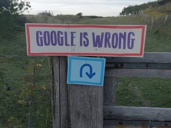 Sign reading 'GOOGLE IS WRONG' tacked to a weathered wooden fence in a rural field.