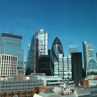 Skyline of modern glass skyscrapers against a clear blue sky, with sunlight reflecting on the façades.