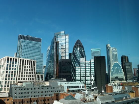 Skyline of modern glass skyscrapers against a clear blue sky, with sunlight reflecting on the façades.
