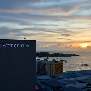 Hotel building with 'Hyatt Centric' sign overlooking a sunset harbor and boats on the water.