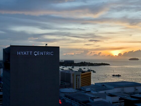 Hotel building with 'Hyatt Centric' sign overlooking a sunset harbor and boats on the water.