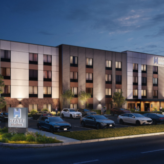 Exterior view of Hyatt Studios hotel at dusk with an illuminated entrance and parked cars in front.