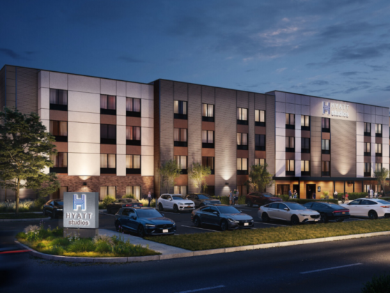 Exterior view of Hyatt Studios hotel at dusk with an illuminated entrance and parked cars in front.