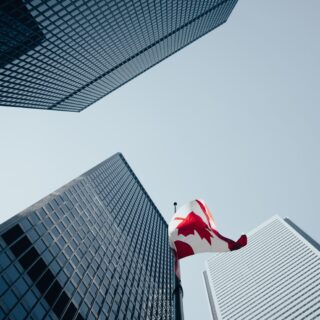 Low-angle view of tall glass skyscrapers with a red-and-white flag fluttering between them against a clear blue sky