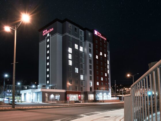 Nighttime exterior of a Hilton Garden Inn with lit windows, streetlights, and a star-filled sky.